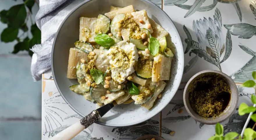 Piatto di pasta ricotta e zucchine, condito con pesto e pinoli, guarnito con basilico fresco.