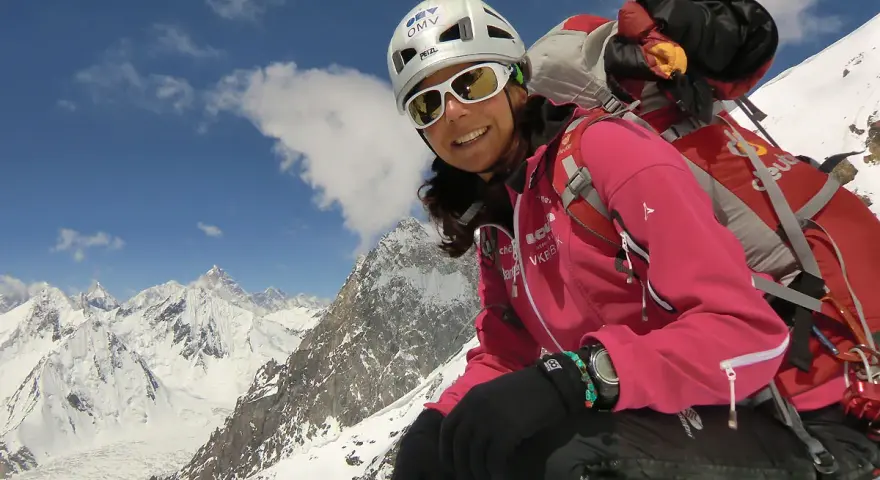 Gerlinde Kaltenbrunner, lächelnd in voller Bergsteigerausrüstung, vor einer majestätischen Schneelandschaft.