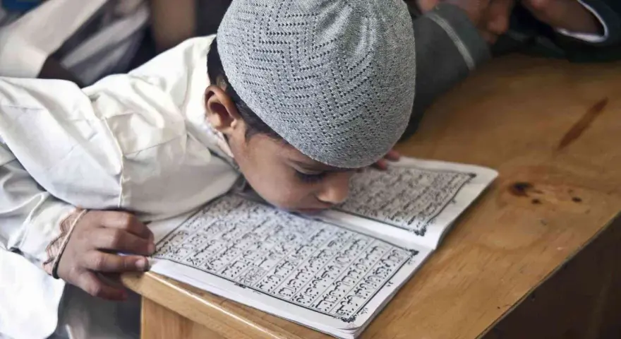 Chłopiec w czapce na głowie pochyla się nad Kor'anem, ucząc się o senegalskiej religii.