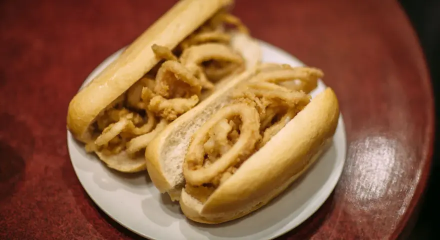 Dos bocadillos de calamares fritos en pan blanco sobre un plato blanco.