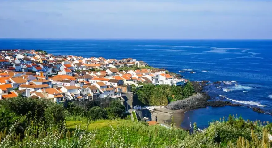 Malownicze miasteczko na wybrzeżu Portugalii, z białymi domami i pomarańczowymi dachami, nad błękitnym oceanem. Ceny wakacji w Portugalii mogą być zaskakująco przystępne.