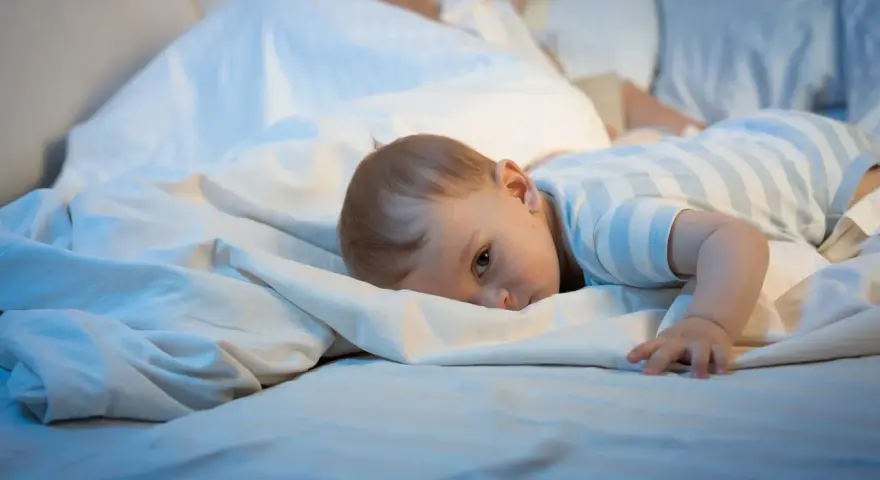 Małe dziecko leży na łóżku, zastanawiając się, dlaczego dziecko budzi się w nocy.