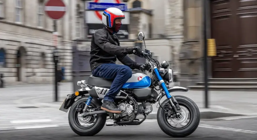 Mężczyzna w kasku jedzie na małym motocyklu, przypominającym boda boda, po ulicy miasta.