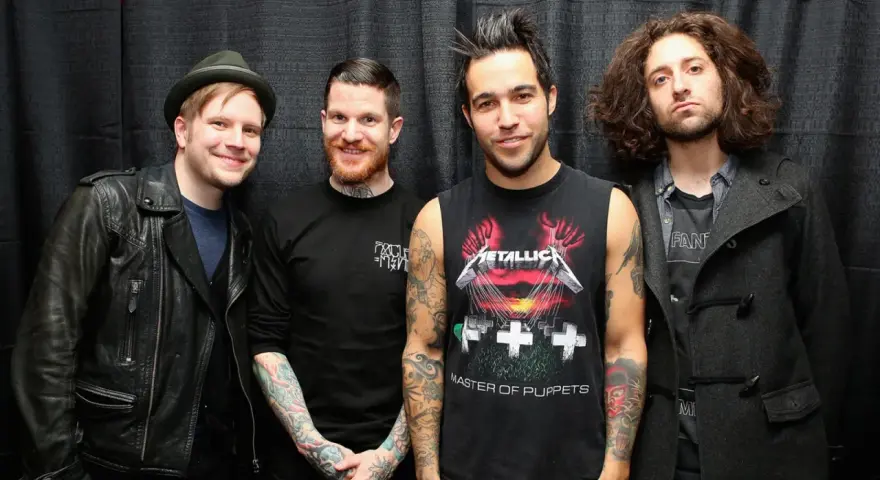 Czterech mężczyzn z zespołu Fall Out Boy pozuje do zdjęcia na tle czarnej kurtyny.