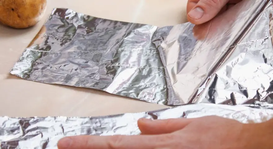 Ręce rozwijają folię aluminiową obok ziemniaków. Zastanawiasz się, gdzie wyrzucić folię aluminiową?