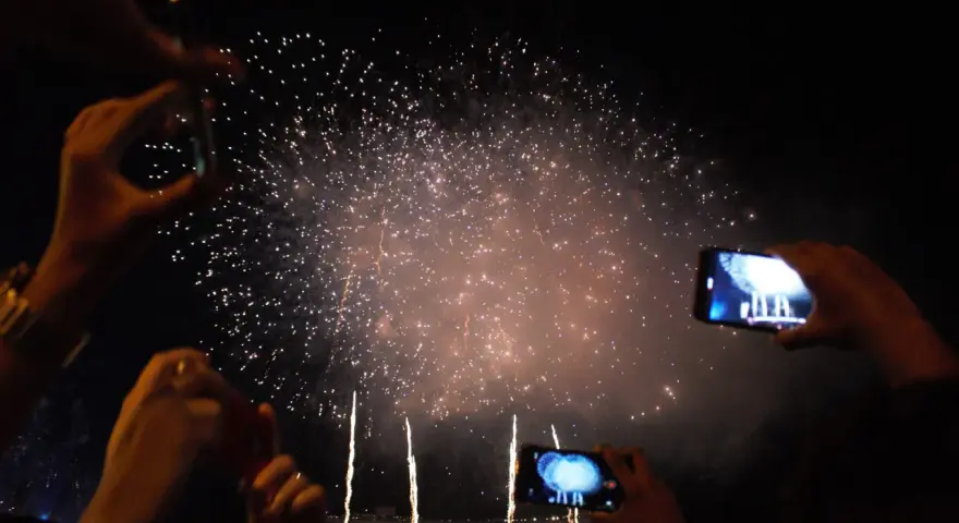 Des mains filment un magnifique feu d'artifice dans le ciel nocturne, capturant la magie de l'instant.