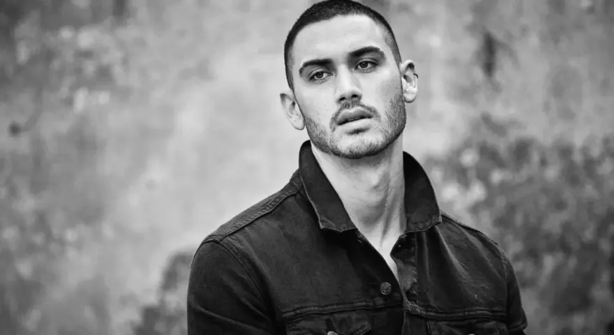 Hombre joven con un corte de pelo buzz cut, viste chaqueta vaquera oscura. Mirada intensa.