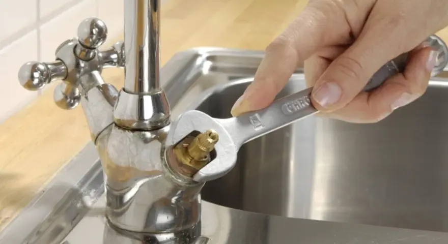 Hand repariert tropfenden wasserhahn mit einem Schraubenschlüssel.