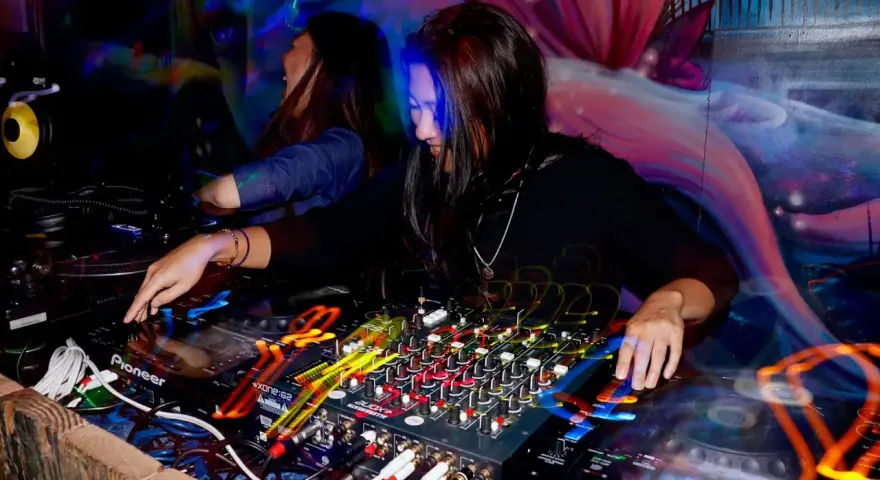DJka miksuje energetyczne rytmy afro house w klubowej atmosferze. Kolorowe światła i dynamiczna muzyka tworzą niepowtarzalny klimat.