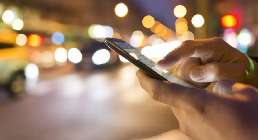 Hände bedienen ein Smartphone im nächtlichen Stadtverkehr. Tipps, um das iPhone schneller machen, sind hier vielleicht gesucht.