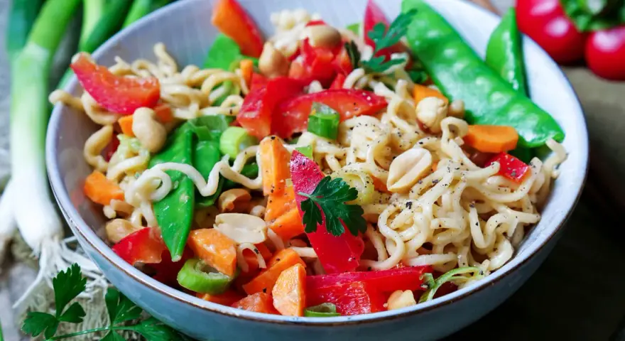 Bunter mie nudelsalat mit Erdnüssen, Zuckerschoten, Karotten und Paprika, garniert mit Petersilie.