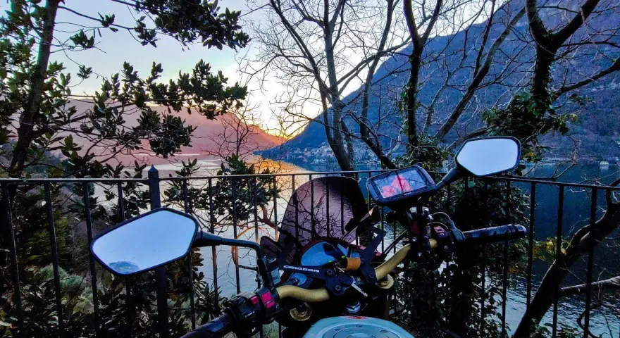 Manubrio moto con vista panoramica sul Lago di Como al tramonto. Un invito a esplorare i punti panoramici in moto.