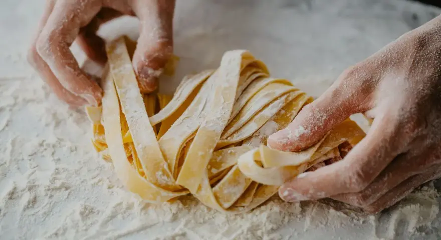 Mani infarinate lavorano un nido di tagliatelle fatte in casa, pronte per essere cucinate.