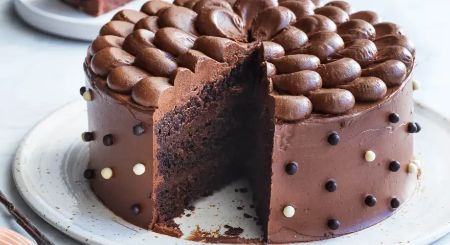 En saftig, klassisk chokladtårta med chokladfrosting och dekorationer av chokladkulor. En bit är bortskuren.