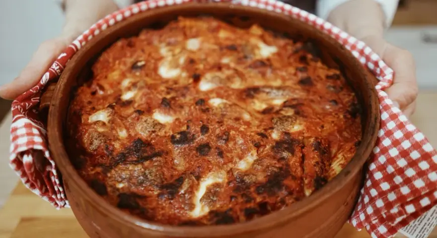 Un invitante pasta al forno ricetta della nonna, appena sfornata in una terracotta, con crosticina dorata e ripieno filante.