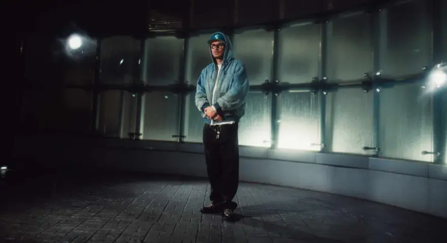 Pezet w niebieskiej kurtce i czapce z daszkiem, stojący w nowoczesnym, przeszklonym wnętrzu. To jego plan B na wieczór.