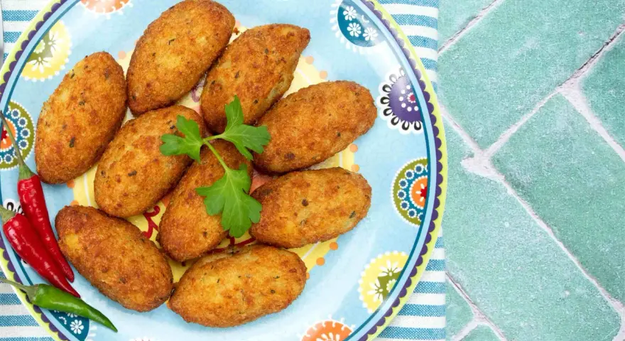 Croquetas doradas en un plato decorado con pimientos y perejil.