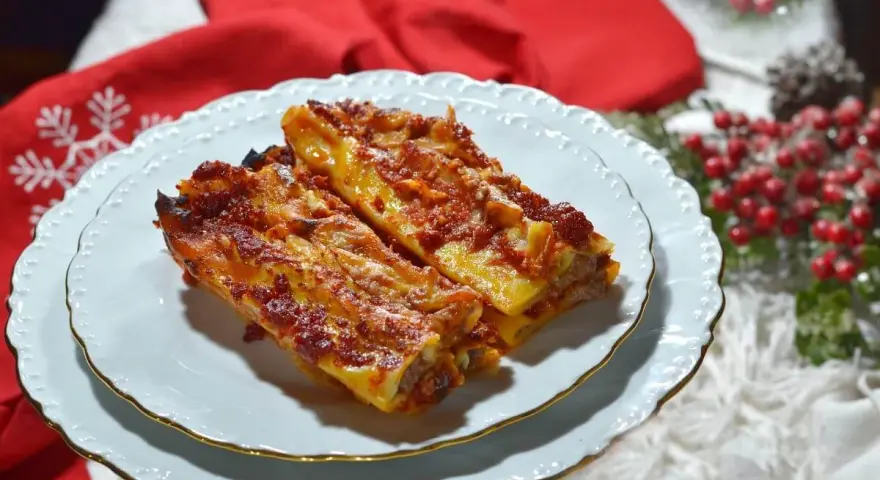 Due cannelloni di carne fumanti, ricoperti di sugo rosso e formaggio filante, serviti su un piatto bianco con bordo dorato, pronti per essere gustati.