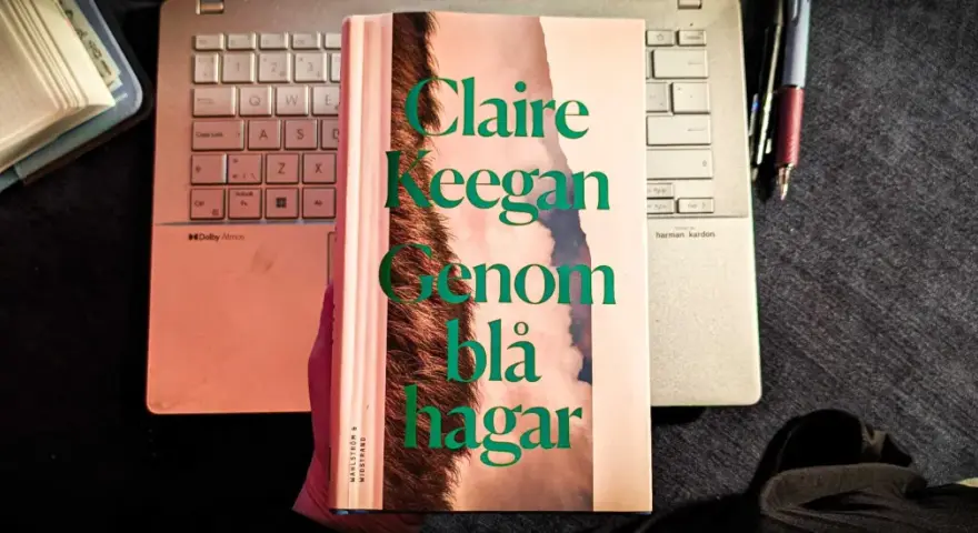 Claire Keegans bok "Genom blå hagar" ligger på ett tangentbord bredvid en anteckningsbok och pennor.