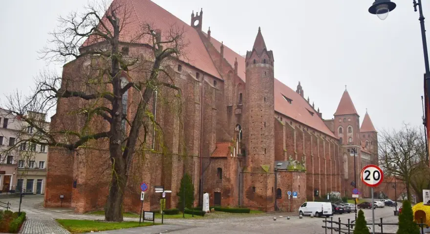Imponująca katedra w Kwidzynie, z cegły, z charakterystycznymi wieżami i czerwonym dachem, otoczona drzewami i budynkami.