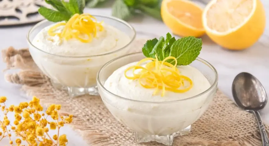 Dos copas de cremoso mousse de limón con leche condensada, decoradas con ralladura de limón y menta.