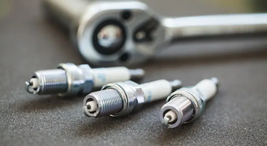 Three spark plugs and a ratchet are laid out, ready for a tune-up. The image highlights the importance of knowing the correct spark plug socket size for the job.