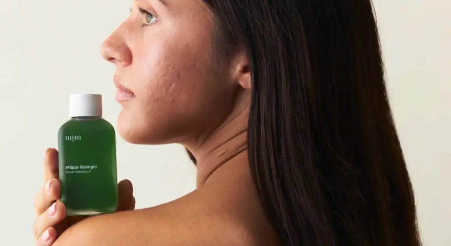Frau hält eine grüne Flasche "Milder Reiniger" für ihre Beauty-Routine.