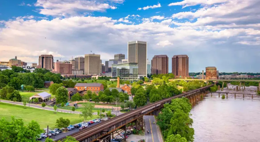 A scenic view of Richmond, VA, showcasing the city skyline, a river, and a railway bridge. Perfect for a weekend getaway.