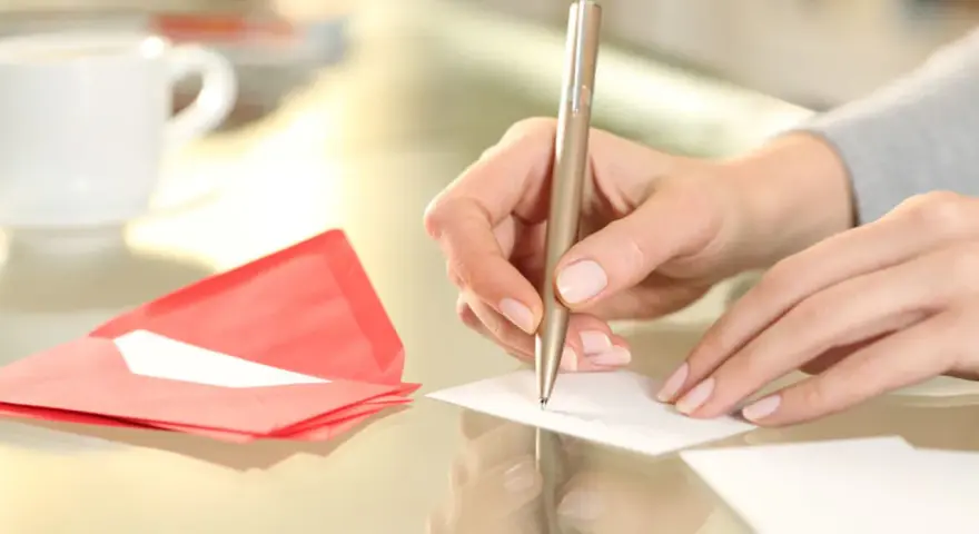 Main tenant rédige un modèle d'autorisation parentale TAM. Une tasse de café et une enveloppe rouge sont à proximité.
