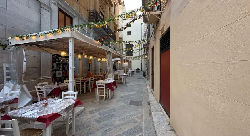 Urocza uliczka w Trapani, gdzie zjeść? Stoliki restauracyjne pod girlandami z cytryn i lampek, idealne na wieczorny posiłek.