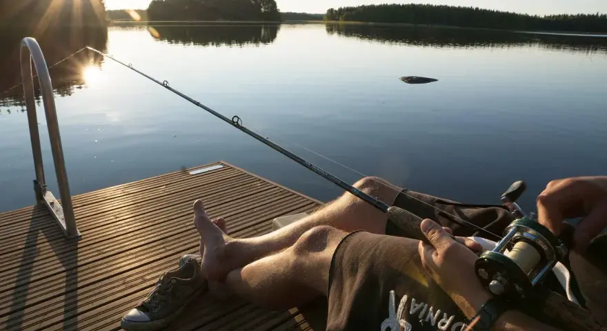 Spokojny dzień nad jeziorem Urszulewskim. Wędkarz czeka na branie, słońce zachodzi, odbijając się w spokojnej tafli wody.