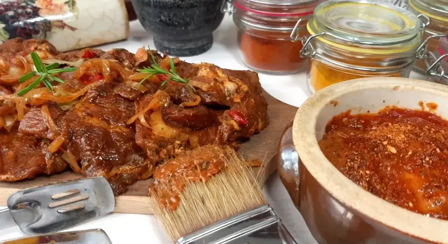 Karkówka na grilla w aromatycznej marynacie, gotowa do pieczenia. Obok pędzel z marynatą i słoiczki z przyprawami.