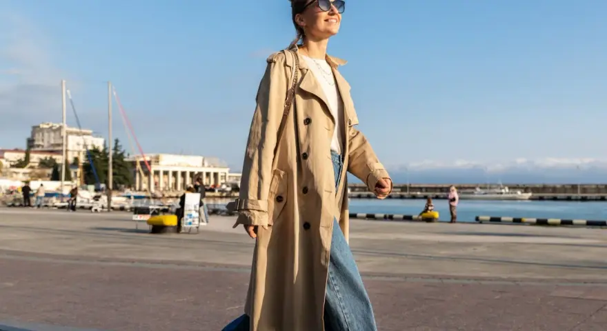 Una chica con estilo, con un look clean girl, pasea por el puerto con un abrigo beige y vaqueros anchos.