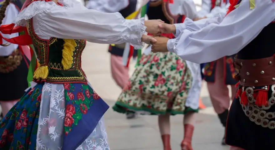 Tancerze w barwnych strojach ludowych, żywa muzyka folkowa w tle.
