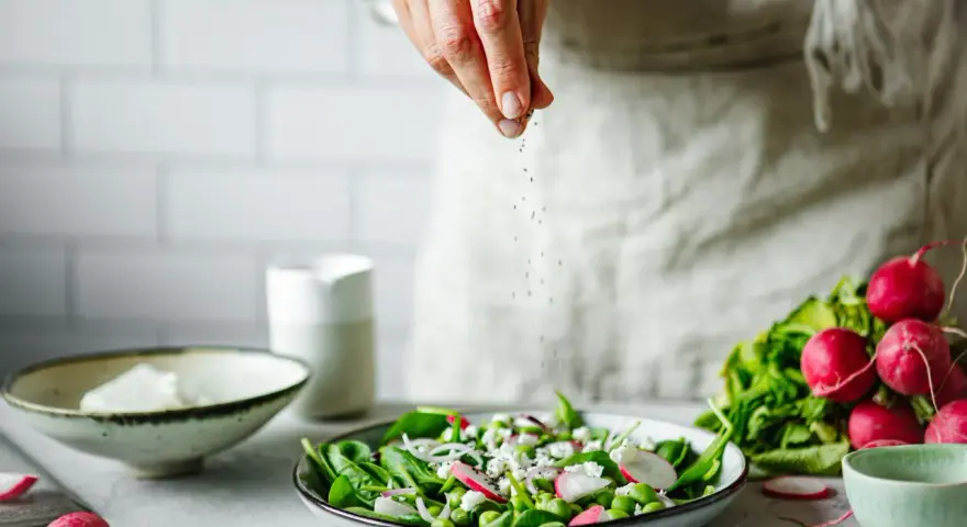 Une main saupoudre des graines sur une salade fraîche. Une idée pour une recette de radis noir.