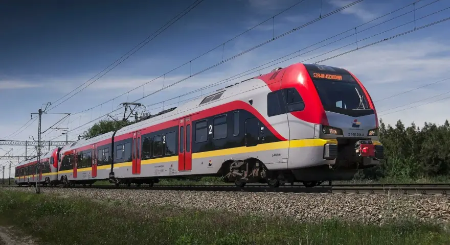 Nowoczesny pociąg do Łodzi mknie po torach wśród zieleni.
