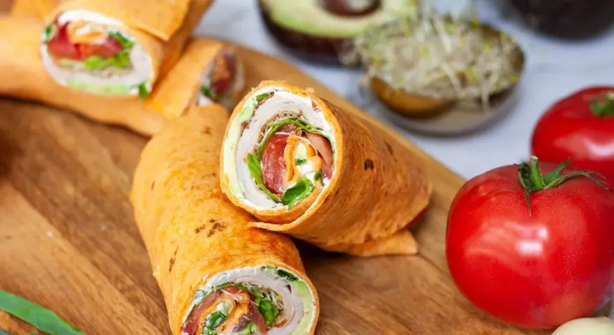 Pyszna tortilla na śniadanie z warzywami i kremowym serkiem. Obok pomidory, awokado i kiełki.