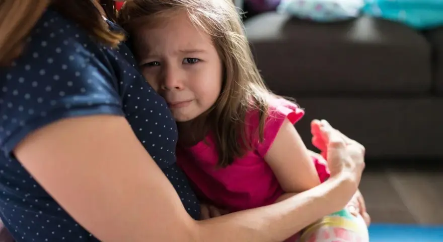 Mała dziewczynka płacze, wtulona w mamę. To właśnie parenting – trudne chwile i bezwarunkowa miłość.
