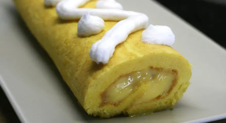 Un brazo de gitano amarillo con relleno cremoso y merengue blanco decorando la superficie.
