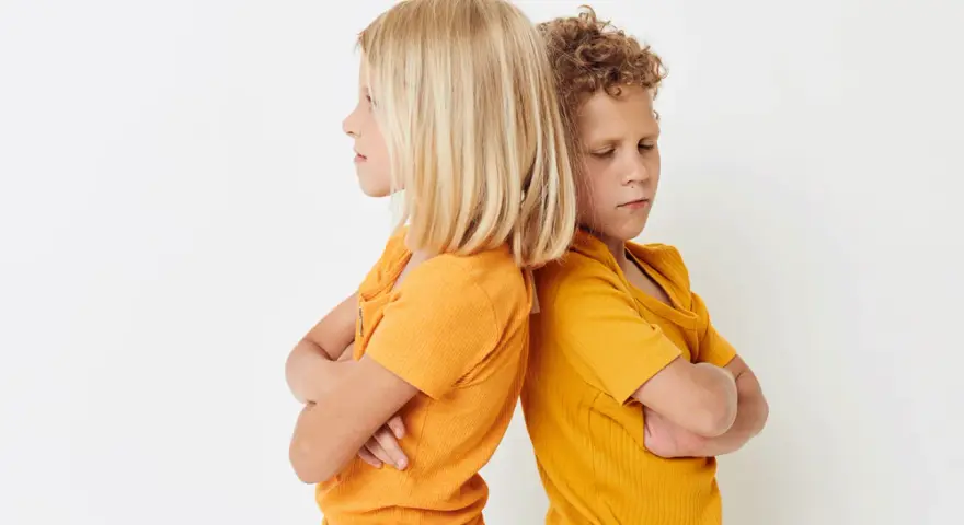 Zwei Kinder stehen mit verschränkten Armen Rücken an Rücken. Ihre Mimik deutet auf **Gewalt unter Geschwistern** hin, ein Streit, der sie trennt.