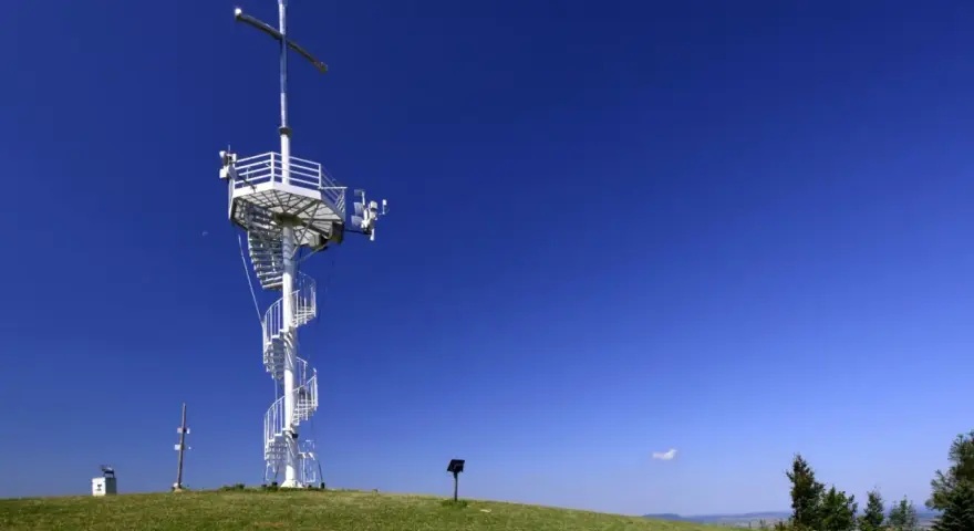 Wieża widokowa na górze Grzywackiej z krzyżem i spiralnymi schodami, na tle błękitnego nieba.