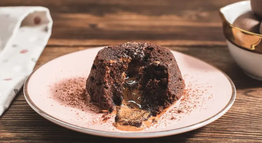 Coulant de chocolate con centro líquido y cremoso, espolvoreado con cacao en polvo sobre un plato rosa.