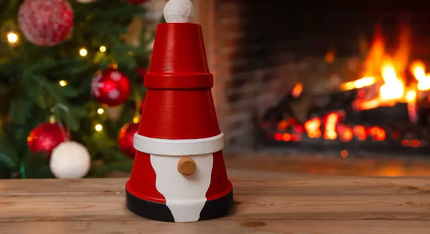 En söt tomte gjord av krukor står framför en sprakande brasa och en julgran. Perfekt för att måla tomte-pyssel.