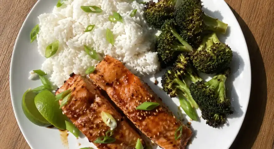 Två saftiga filéer av asiatisk lax serveras med fluffigt ris, rostad broccoli och limeklyftor.