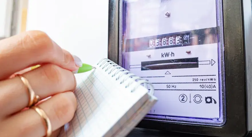 Dłoń z pierścionkami zapisuje odczyt licznika energii elektrycznej, by sprawdzić rachunek za prąd.