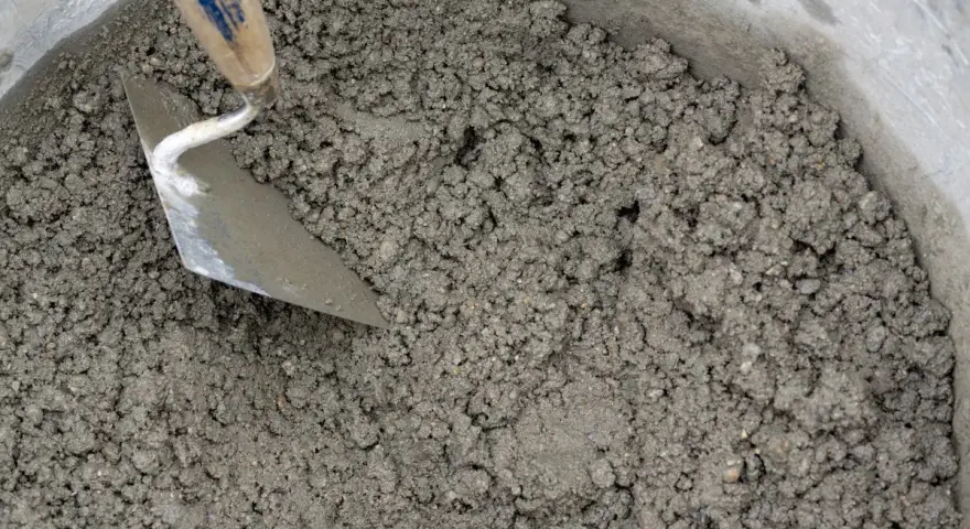 Una cazzuola mescola la malta appena preparata in un secchio. Ecco come fare la malta per i tuoi progetti.