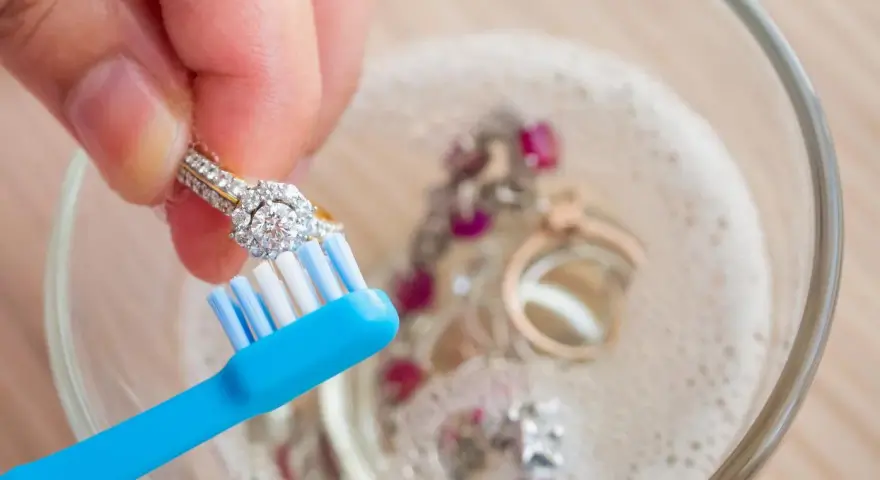 Limpia tu plata con bicarbonato y vinagre. Un anillo de diamantes se cepilla suavemente en un bol con joyas burbujeantes.