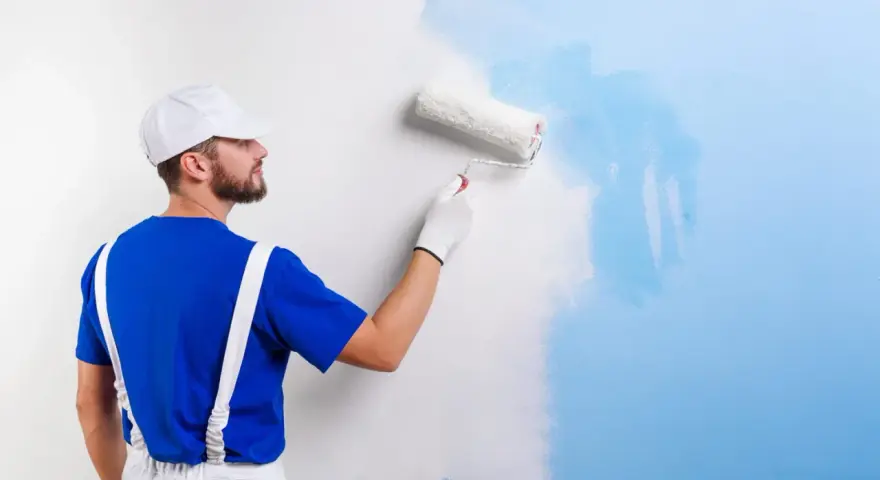 Un peintre en bleu et blanc applique une nouvelle couche de peinture bleue sur un mur blanc. C'est une peinture sur peinture en cours.