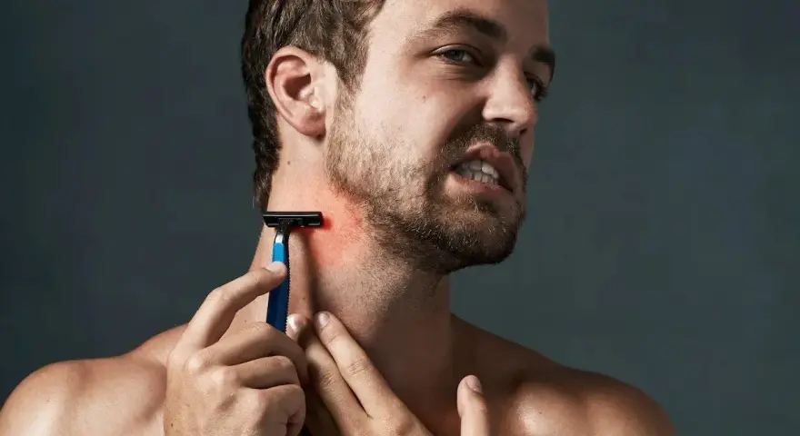 Hombre con piel irritada afeitado, se rasca el cuello con una navaja de afeitar azul.