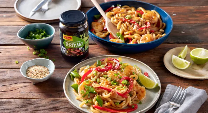 Krewetki z makaronem w sosie teriyaki, podane na talerzu z dodatkami.